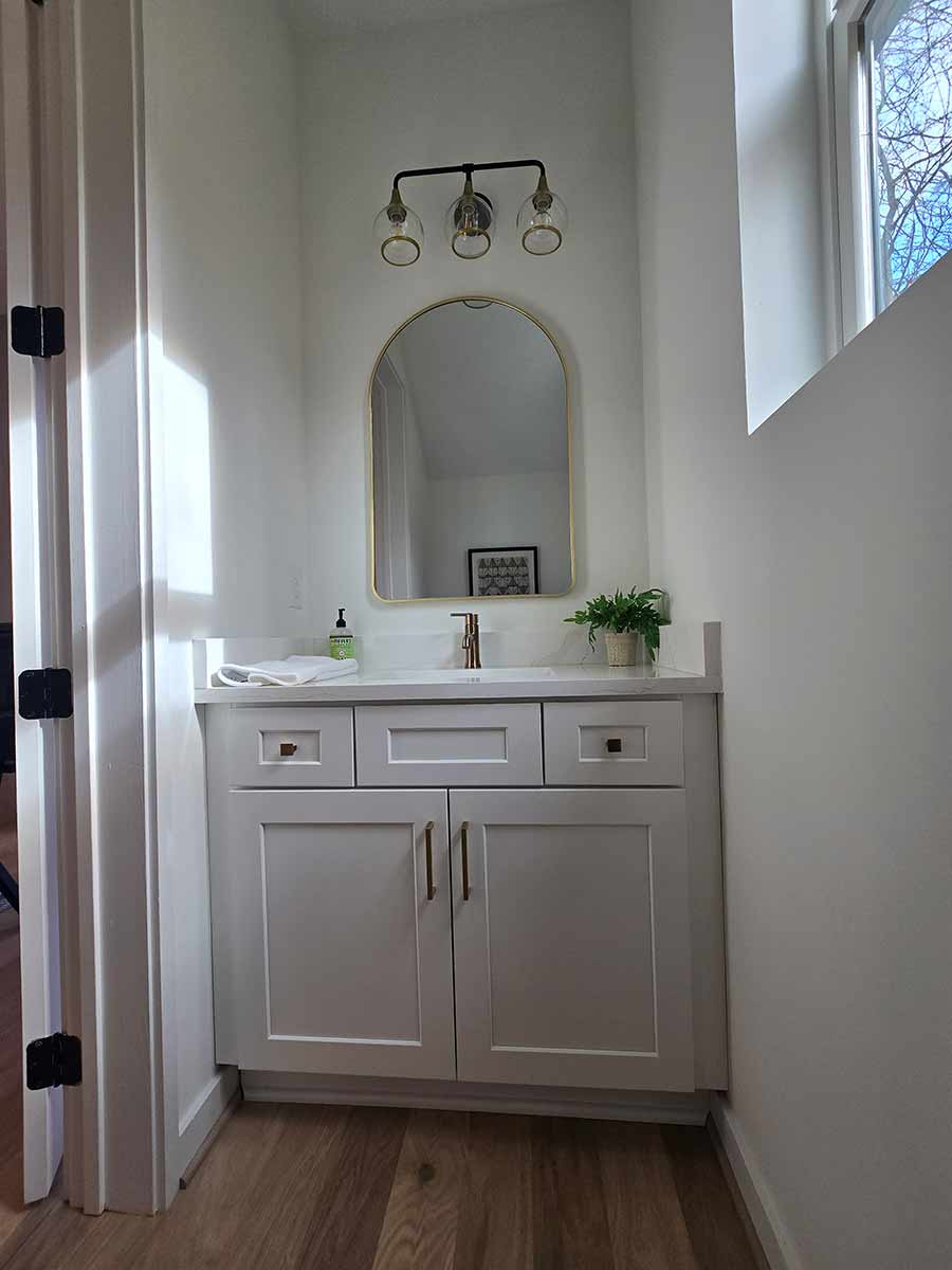 Powder bathroom renovation with arched brass mirror and shaker vanity